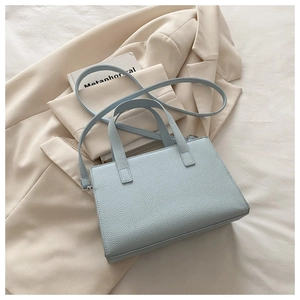 Detail of light blue lychee pattern leather handbag placed on a beige blazer