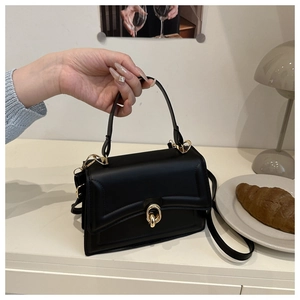 Detail of classic black leather handbag featuring a stylish gold circular metal twist lock