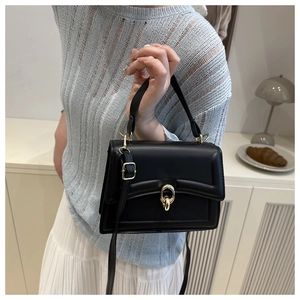 Detail of black faux leather bag featuring a distinct golden circular metal buckle and strap