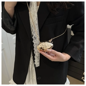 Mini gold metallic shell bag with ripple texture and chain strap worn on black suit