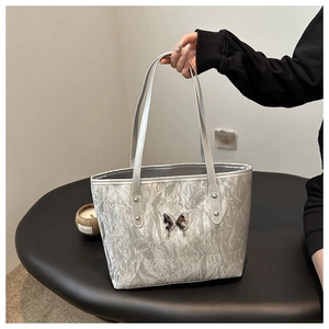Detail of silver metallic tote bag featuring pleated texture and metal butterfly ornament