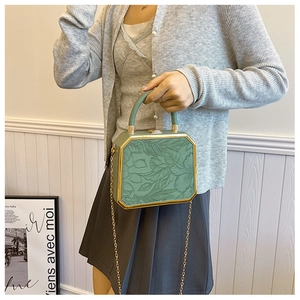 Detail of dark green hexagonal clutch with floral embossing and golden metal trim