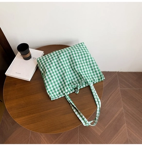 Detailed close-up of green and white plaid tote bag with ribbon bow on wooden table