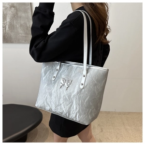 Macro shot of silver pleated tote bag featuring a metallic butterfly buckle and strap