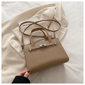 Detail of khaki lychee grain leather bag with metal turn-lock on a beige blazer background