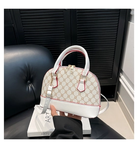 Chic white leather shell bag with red edges and monogram detail on a black leather chair