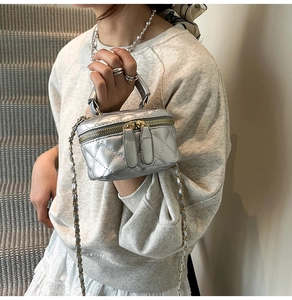 Close-up of silver quilted crossbody bag with dual golden zippers and woven chain strap