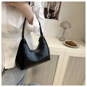 Detail of minimalist black patent leather crescent bag with silver zipper and silver logo