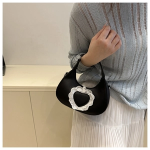 Dettaglio borsa a mezzaluna nera con cuore in pizzo indossata da una modella elegante