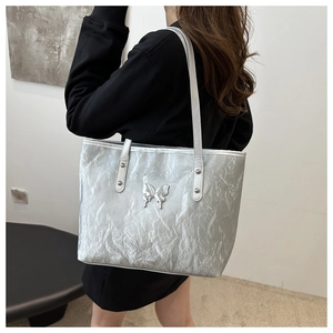 Silver metallic tote bag with pleated texture and butterfly charm detail shown on shoulder
