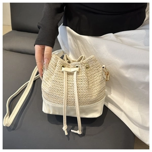 Detailed close-up of straw bucket bag featuring white leather base and drawstring closure