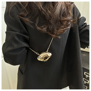 Gros plan d'un mini sac doré en forme de coquille avec chaîne sur une veste noire chic