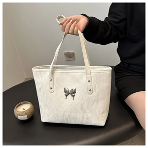 Detail of white pleated tote bag with a metallic silver butterfly accent and shoulder strap