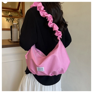 Pink nylon cloud bag with wide pleated shoulder strap worn by a model in a cafe setting