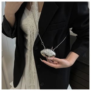 Detailed view of mini metallic shell crossbody bag with silver chain on model outfit
