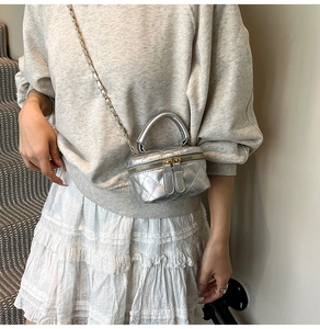 Silberne Mini-Umhängetasche mit Steppmuster, Metallkette und Griff am Modell gezeigt