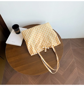 Flat lay of yellow plaid canvas tote bag with bow detail on a round wooden table