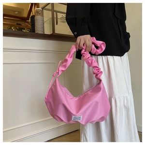 Close-up of pink pleated crescent bag with fashion tag held in a modern cafe setting