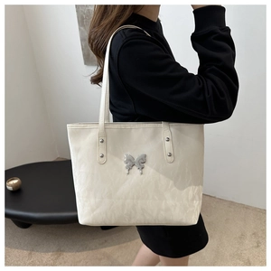 Chic cream tote bag with butterfly metal accent and crinkled texture shown on shoulder