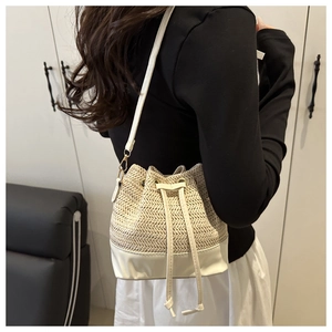 Detail view of woven straw bucket bag with white leather base and drawstring closure