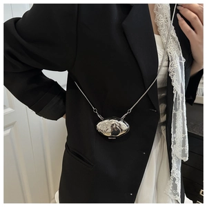 Detail of a silver shell-shaped mini bag with metallic chain shown on a black suit outfit