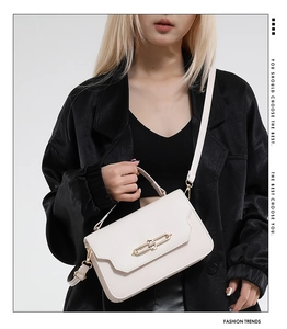 Detail of white structured leather handbag with a prominent gold metal clasp and thin strap