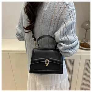 Detail of a minimalist black crossbody bag with a golden ring clasp on a stylish model
