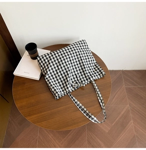 Flat lay of black and white gingham canvas tote bag on a wooden table with coffee cup