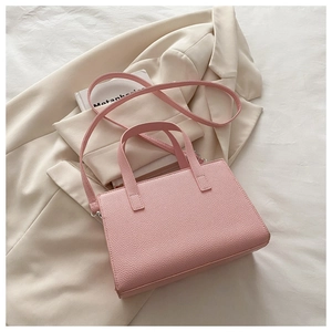 Detail of light pink lychee grain faux leather handbag with dual handles and long shoulder strap