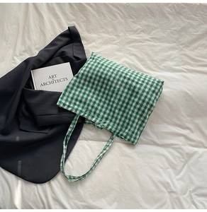 Detail shot of green and white plaid canvas tote bag styled with blazer and art book