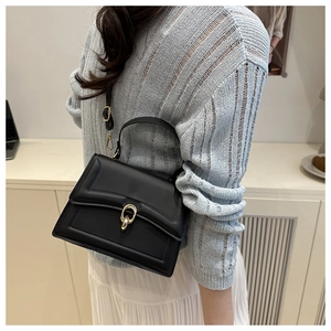Detail of black crossbody bag with golden buckle on a model in a natural setting