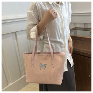 Detail of light pink tote bag with silver butterfly emblem and pebbled texture leather