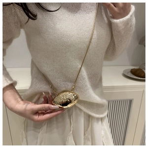 Detail of a golden shell mini crossbody bag with a unique hammered metal texture and chain