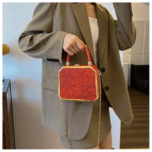 Detail of red octagonal handbag with floral embossing and gold metal chain strap
