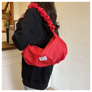 Détail du sac croissant en nylon rouge avec bandoulière plissée et écusson discret