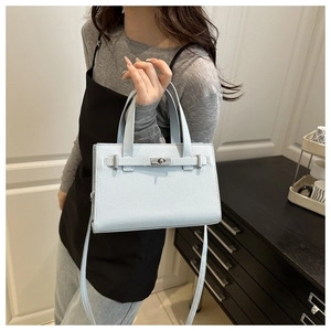 Detailed view of light blue leather handbag with silver turn-lock and fine grain texture
