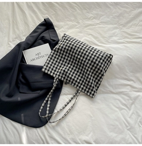 Detailed flat lay of black and white checkered tote bag on minimalist white fabric