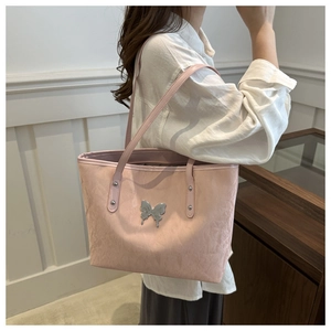 Pink textured leather tote bag with bow detail worn by a model in a casual white shirt