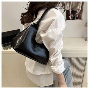 Glossy black crescent shoulder bag shown in a modern urban office setting with model