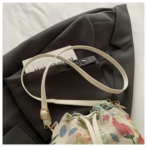 Detail of embroidered strawberry pattern on a cream bucket bag with gold hardware