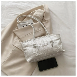 Detail of white lace tote bag with 3D butterfly embroidery on a beige blazer background
