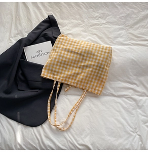 Detail of yellow plaid tote bag styled on white fabric with a blazer and book