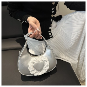 Detail of silver crescent bag with lace heart motif held by a model in elegant attire
