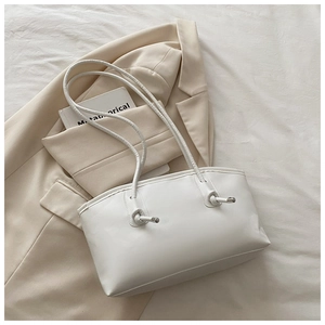 Close-up of white minimalist tote bag with knot detail and silver buckle on beige blazer
