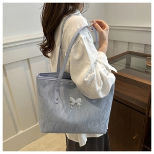 Detail of light blue pleated tote bag with a metallic butterfly charm on shoulder