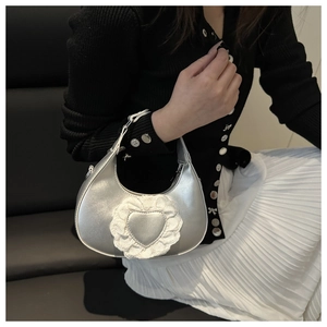 Close-up of a silver crescent handbag with heart detail and white lace trim