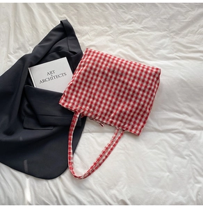 Detail of red gingham cotton tote bag lying on white bedding with art books