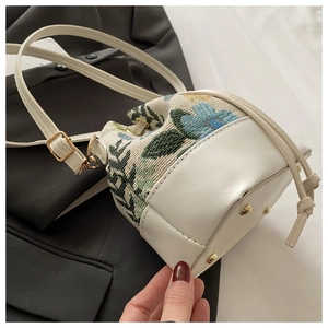 Detail view of ethnic floral embroidery and white synthetic leather on drawstring bucket bag