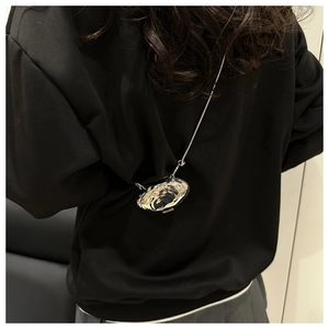 Détail d'un mini sac argenté en forme de coquille avec chaîne sur tenue noire