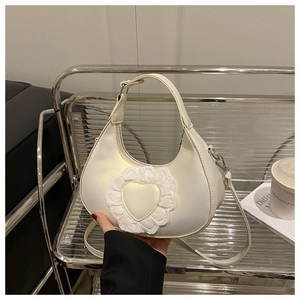 Detail of a creamy white half-moon bag featuring lace heart decor and adjustable strap